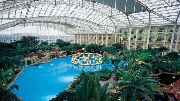 An indoor pool with a glass ceiling, surrounded by lush greenery and a central island. - Grand Metropark Longxi Conference Center Beijing (Daxing)