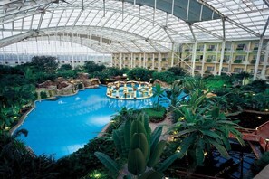 An indoor pool with a glass ceiling, surrounded by lush greenery and a central island. - Grand Metropark Longxi Conference Center Beijing (Daxing)