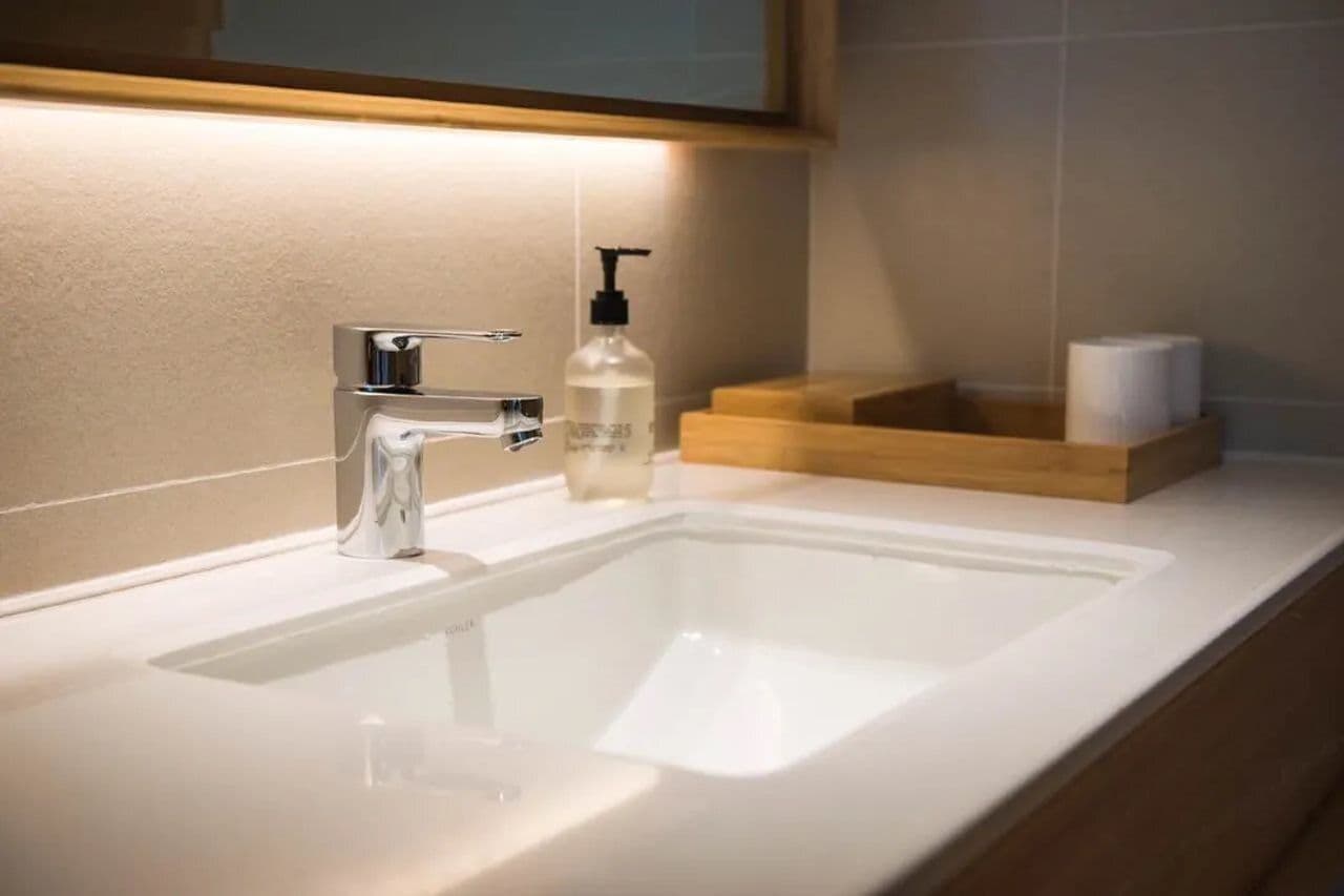 A modern bathroom with a white sink, chrome faucet, and a soap dispenser.