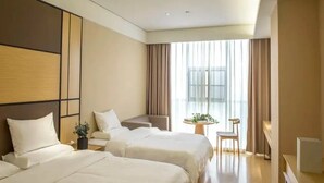 Hotelkamer met twee bedden, een zithoek, een tafeltje met een plant en uitzicht op het groen door grote ramen.