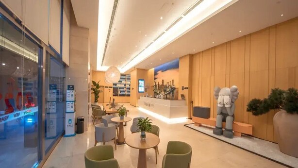 Een moderne hotellobby met een receptiebalie, een zithoek en een groot decoratief beeld.