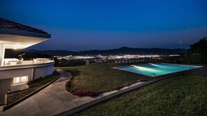 A pool with a view of a city at dusk, a patio area, and a building with a sloped roof. - BASQUE BREATH-Unique Villa, Fantastic View, Fabulous Pool (hondarribia)
