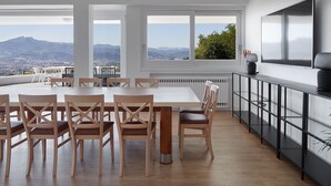 A modern dining area with a large table and chairs, a black console table, and a view of the mountains through large windows. - BASQUE BREATH-Unique Villa, Fantastic View, Fabulous Pool (hondarribia)