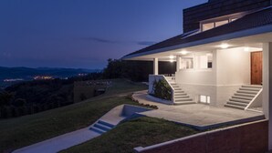 A modern house with a covered porch, a staircase leading to the entrance, and a view of the surrounding landscape. - BASQUE BREATH-Unique Villa, Fantastic View, Fabulous Pool (hondarribia)