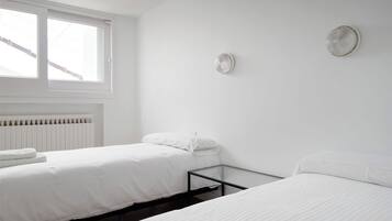 A minimalist bedroom with two beds, a radiator, and a window.