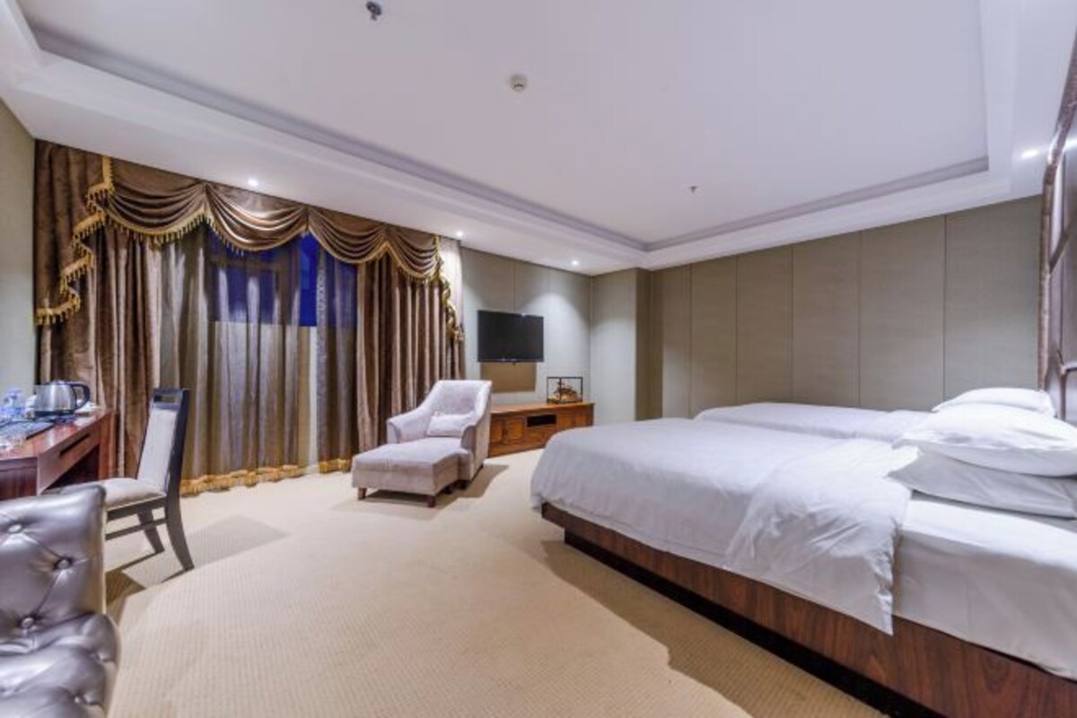 Habitación de hotel con una cama grande, un escritorio con silla, un sillón pequeño y un televisor en la pared.