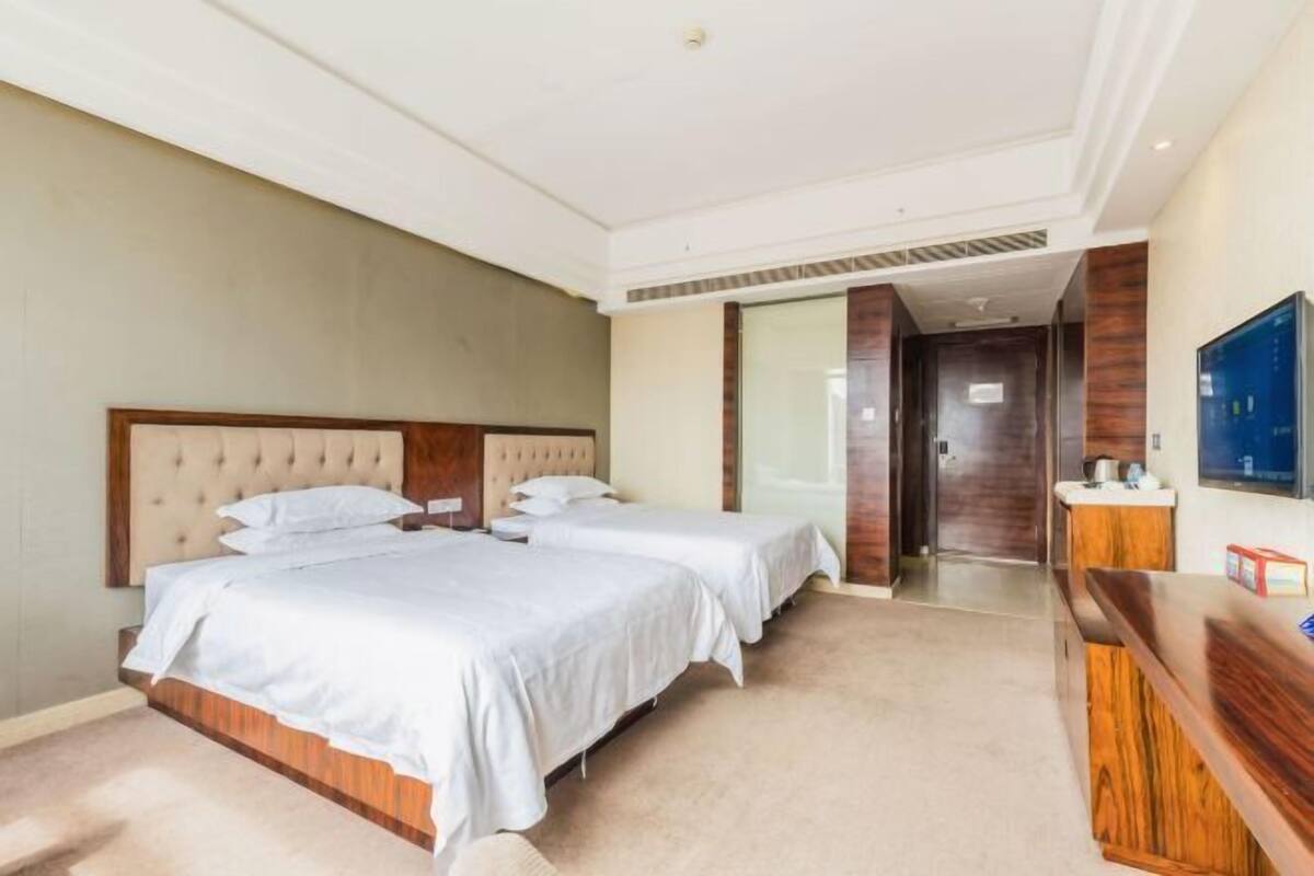 Une chambre d’hôtel avec deux lits, une tête de lit en bois, un téléviseur à écran plat et un comptoir de réception.