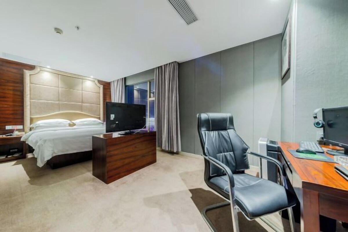 A modern hotel room with a bed, a desk with a computer, a chair, and a television.