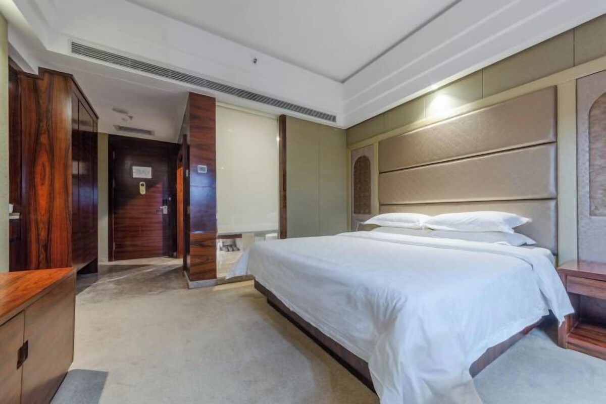 Habitación de hotel con una cama grande, un armario de madera, un escritorio y una puerta que da a otra habitación.
