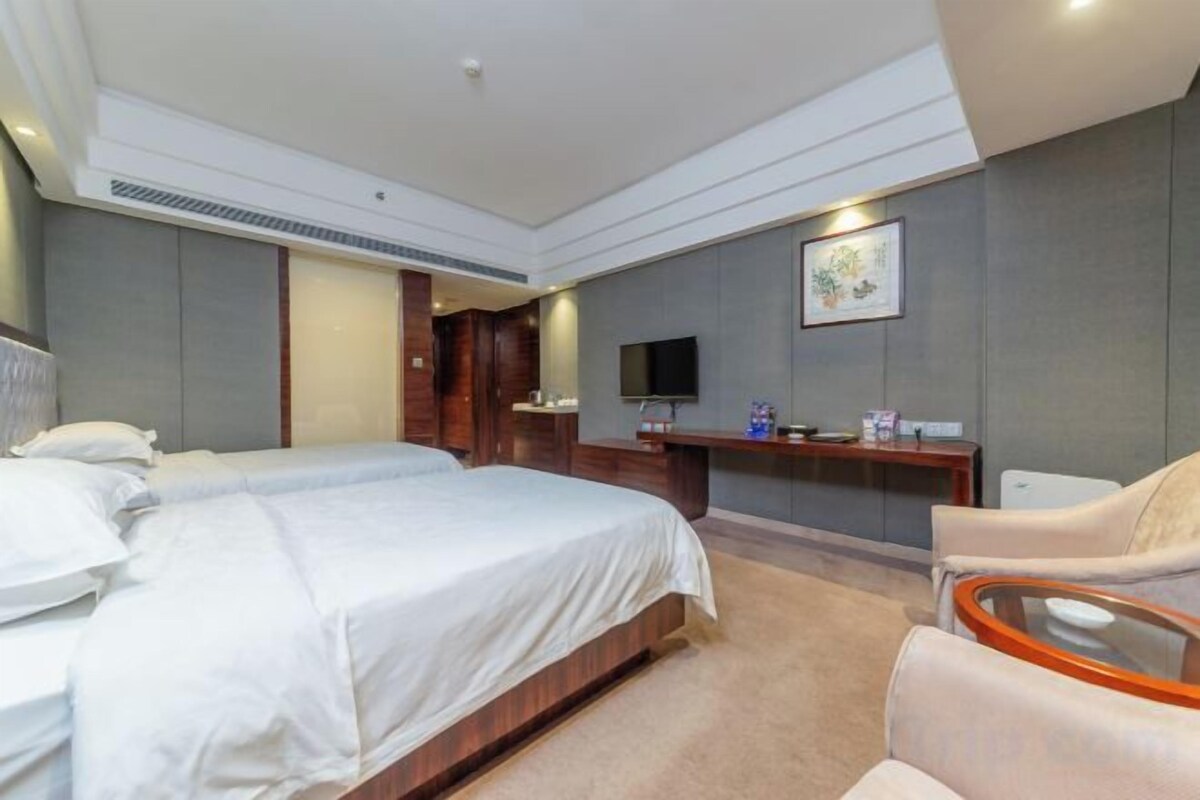 Habitación de hotel con dos camas, un escritorio, un televisor y un espacio para sentarse.