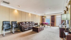 A spacious living room with a leather sofa, two armchairs, a coffee table, and a desk with a lamp. - Jiuzhou International Hotel (Yangxi)