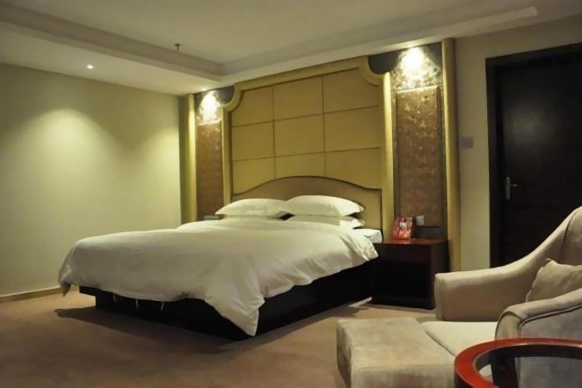 Habitación de hotel con una cama grande, una silla, una mesita y una puerta.