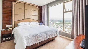 A hotel room with a large bed, a wooden headboard, a nightstand, and a view of a cityscape through a large window. - Jiuzhou International Hotel (Yangxi)
