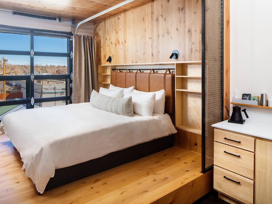 A bedroom with a large bed, wooden headboard, and a white bedside table with a kettle.