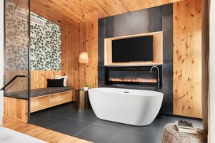 Un baño moderno con una bañera independiente, un banco de madera, un televisor montado en la pared y una chimenea.