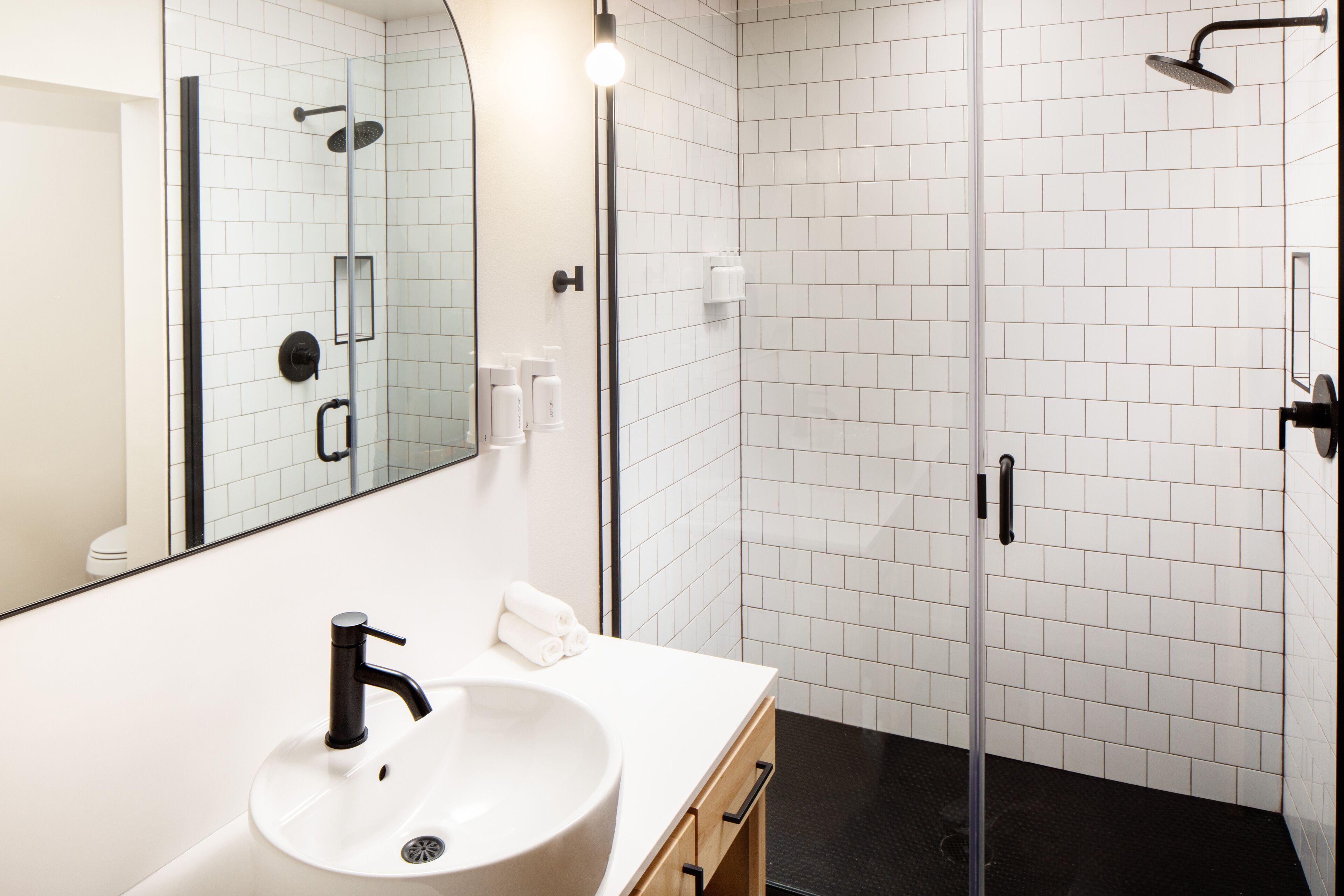A modern bathroom with a white sink, a large mirror, a glass-enclosed shower, and white tiled walls.