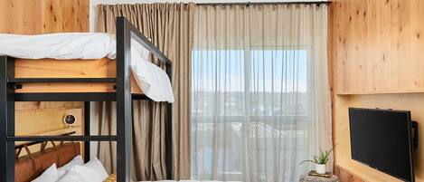A bunk bed room with a wooden ceiling and walls, a television on the wall, and a window with curtains.