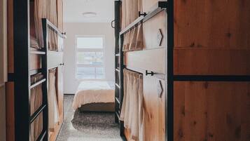 A narrow hallway with bunk beds on either side, leading to a single bed room with a window.
