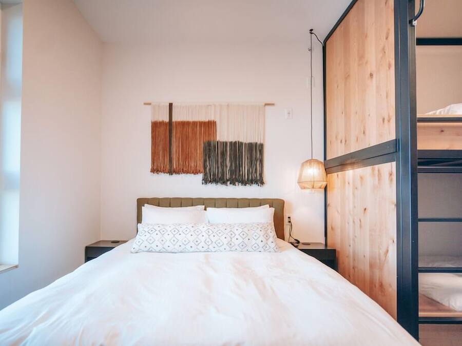 Quarto com beliche, mesa de cabeceira, abajur e janela.