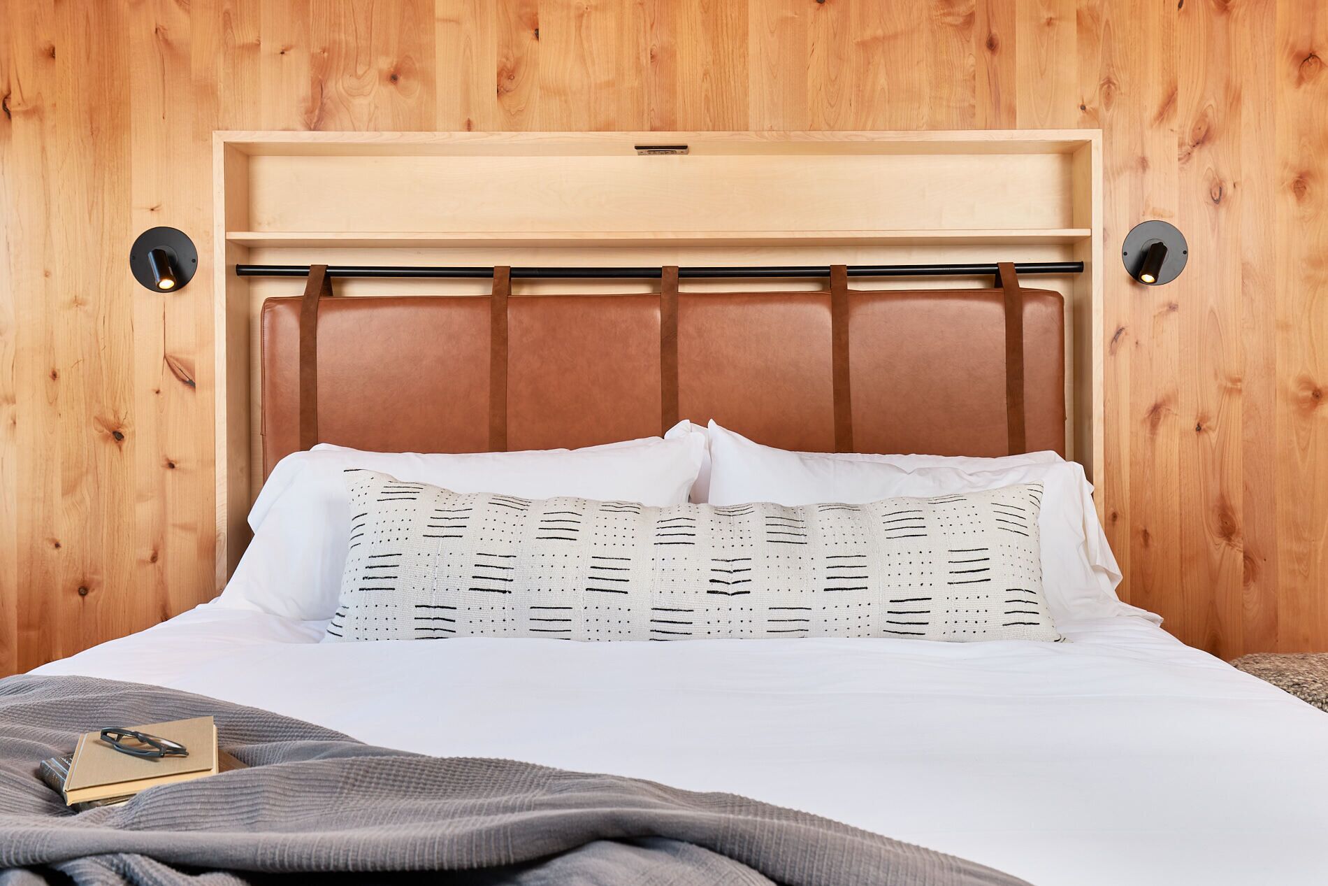 A bed with a wooden headboard, white bedding, and a patterned pillow.