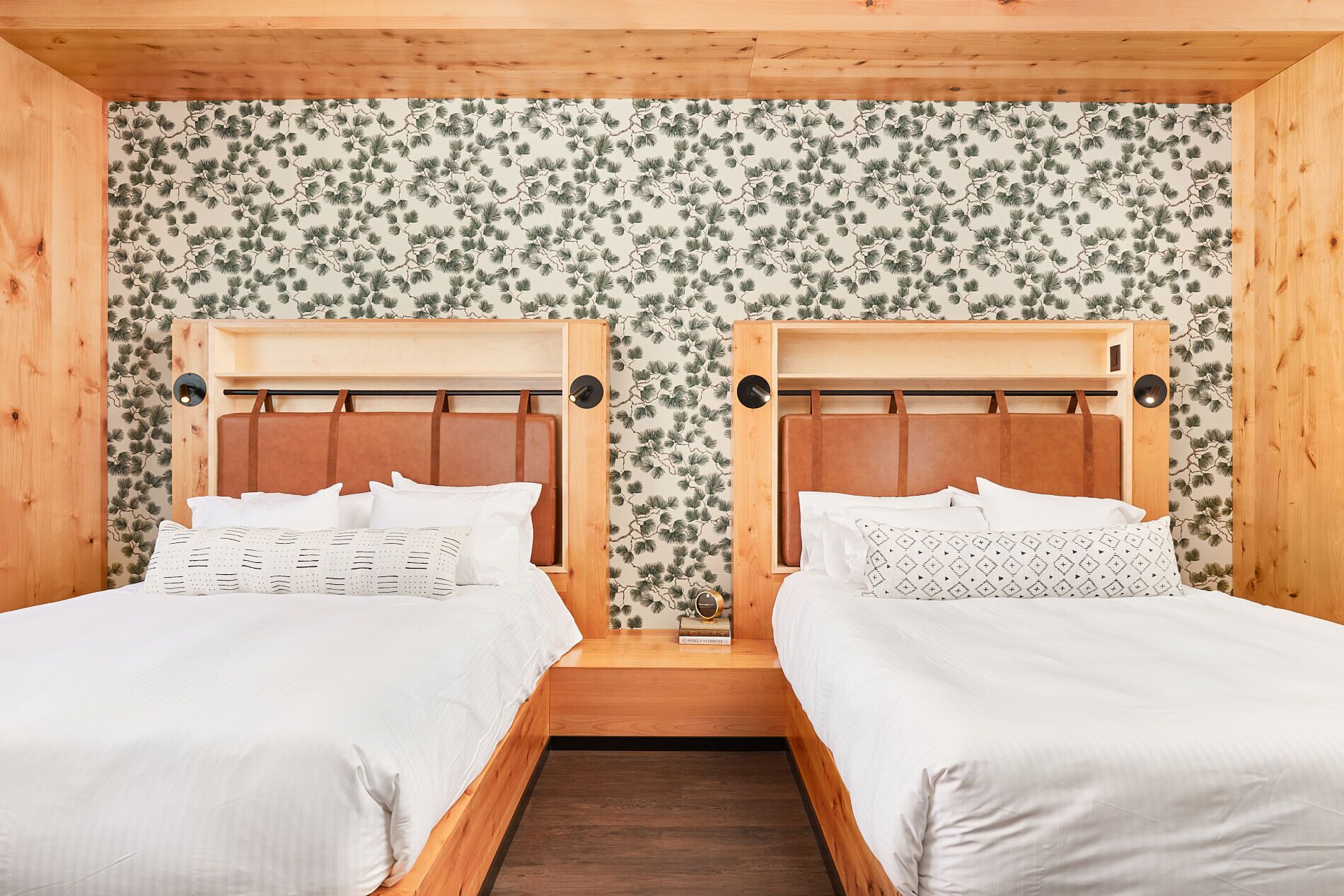 A room with two beds, wooden headboards, and a floral wallpaper pattern.