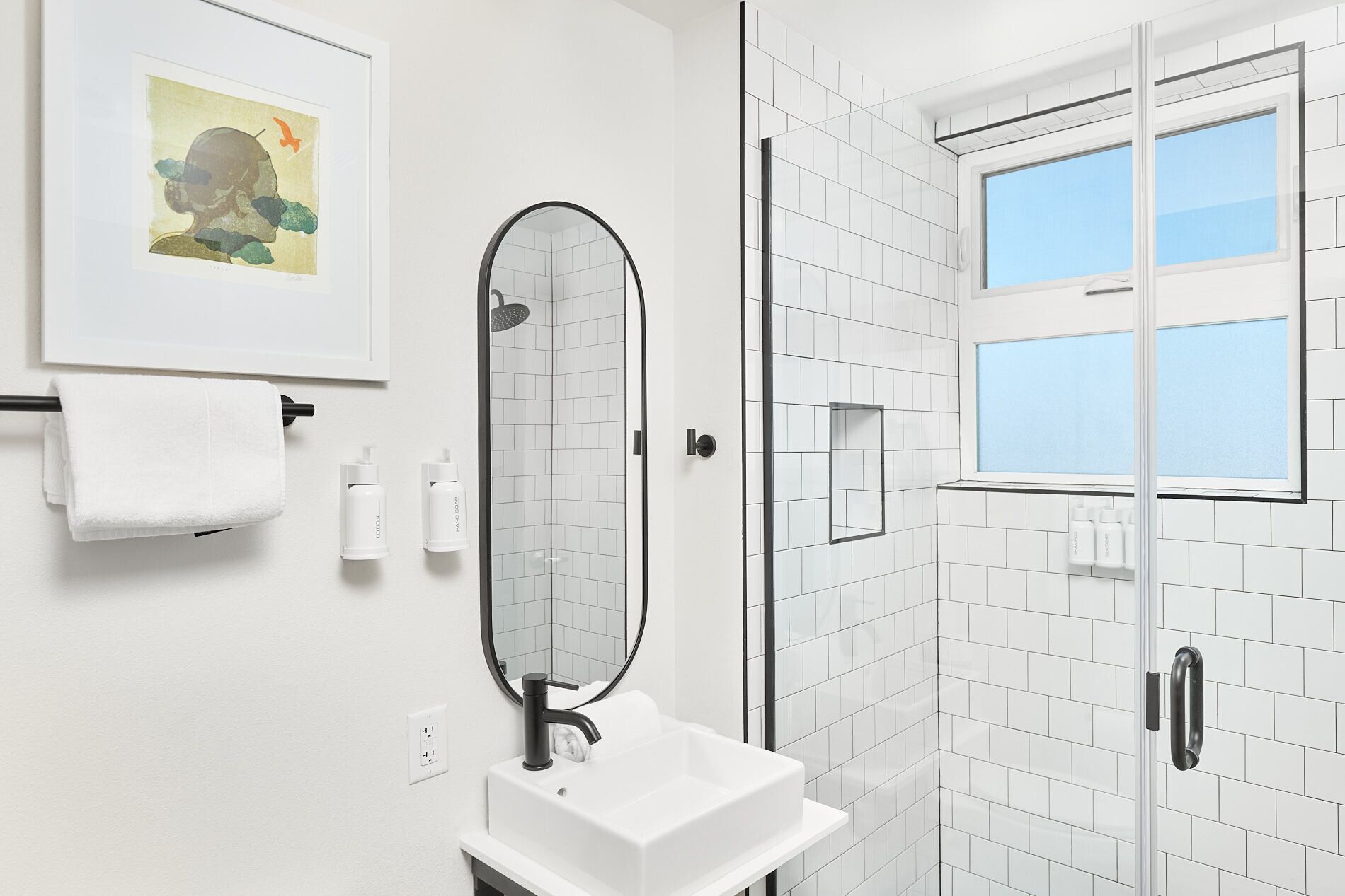 A bathroom with a white sink, a mirror, a shower with a glass door, and a window.