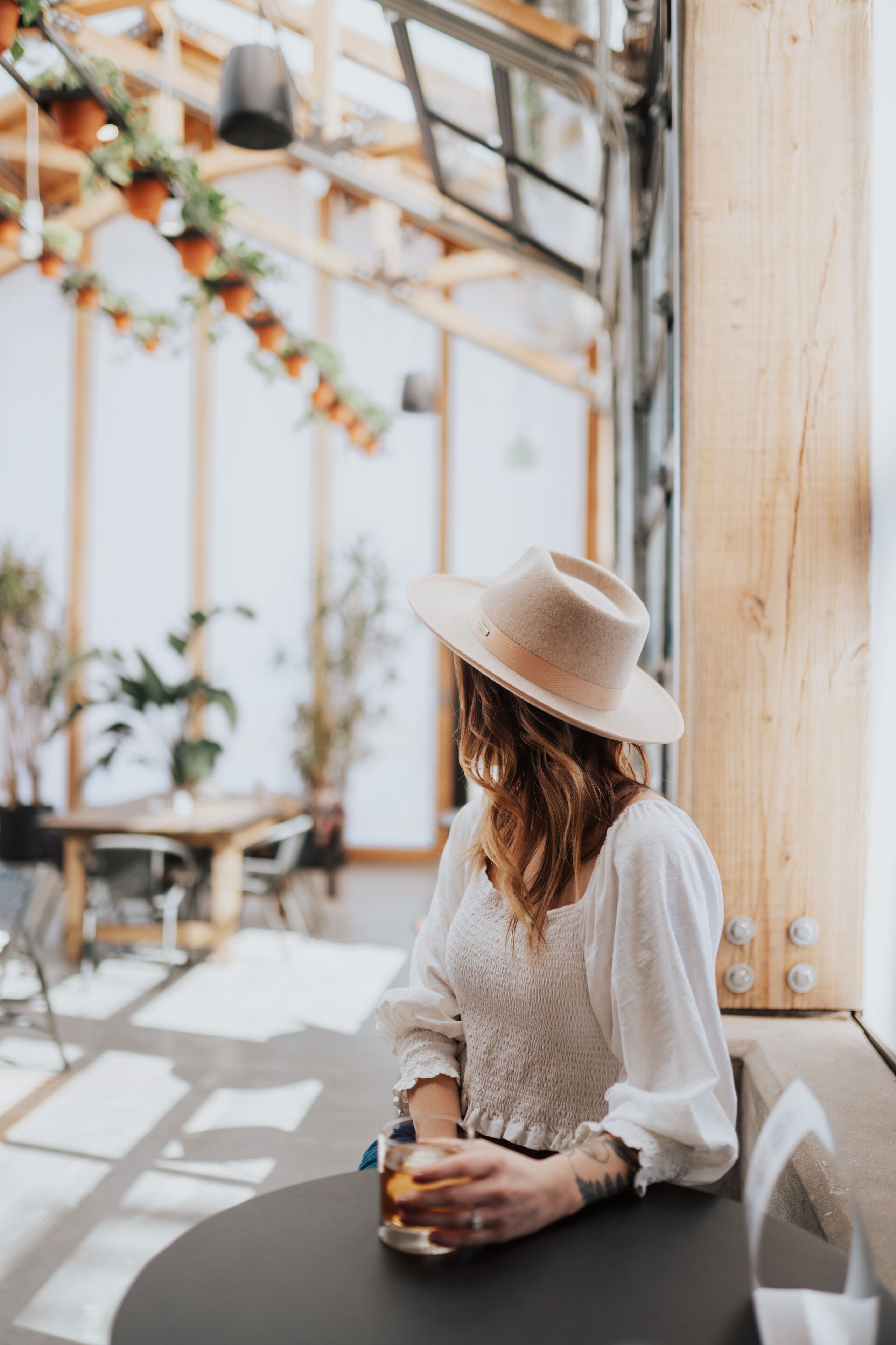 A person seated at a table inside a building with wooden beams and hanging plants.