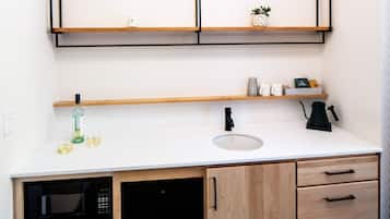 Una cocina compacta con microondas, pileta y alacenas de madera.