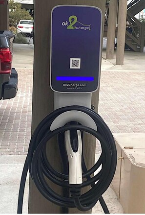 Una estación de carga para vehículos eléctricos, con un código QR y un cable conectado a un automóvil.