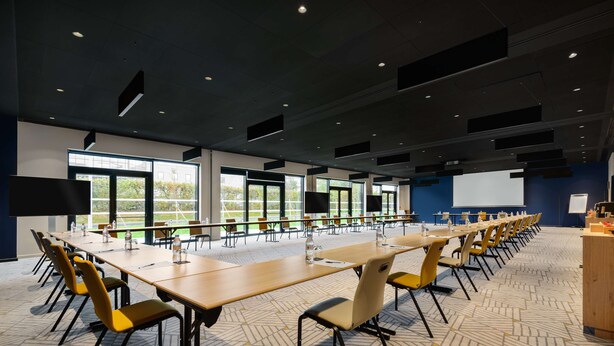 A conference room with long tables, yellow chairs, and a projector screen. - Hyatt Place Paris Charles de Gaulle Airport (Roissy-en-France)