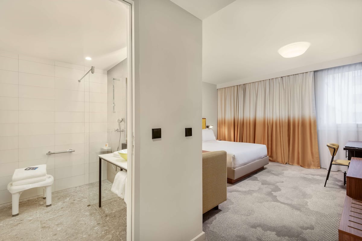 A hotel room with a shower, a bed, a desk, and a chair.
