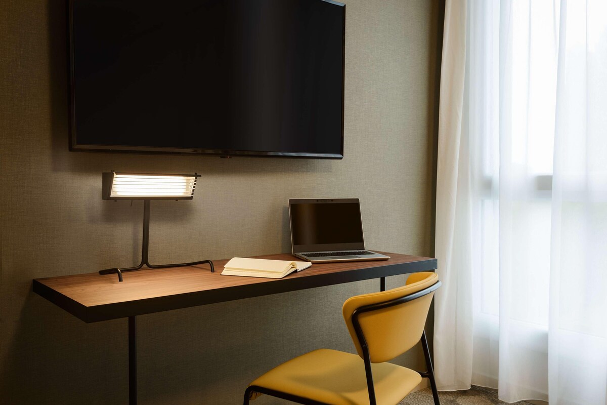 Una habitación de hotel con un escritorio, una computadora portátil, un televisor y una silla.
