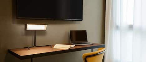 A hotel room with a desk, a laptop, a notebook, a chair, and a TV mounted on the wall.
