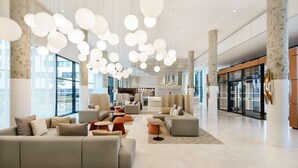 A spacious lobby with a modern design, featuring a large sectional sofa, multiple seating areas, and a central coffee table. - Hyatt Place Paris Charles de Gaulle Airport (Roissy-en-France)