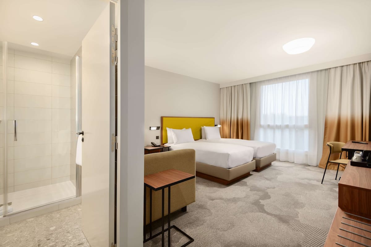 A hotel room with a shower, two beds, a desk, and a chair.