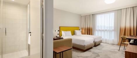 A hotel room with a shower, two beds, a desk, and a chair.