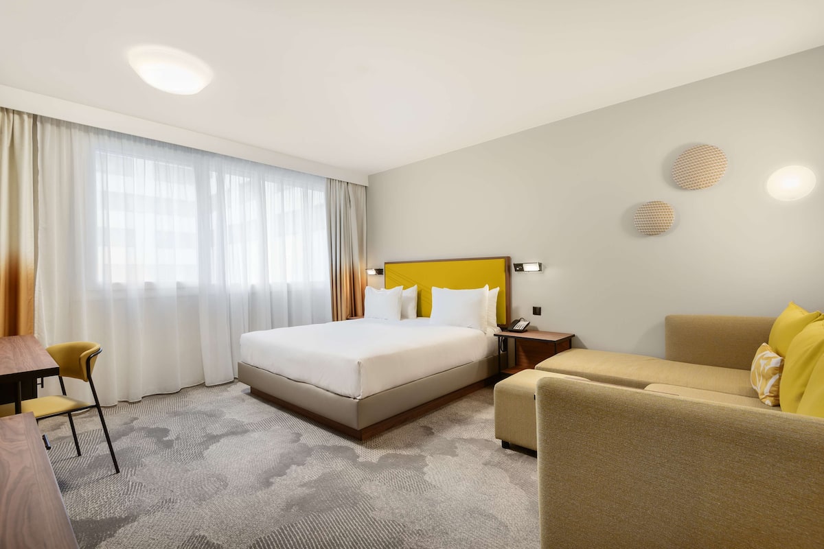 A hotel room with a large bed, a sofa, a desk, and a chair.