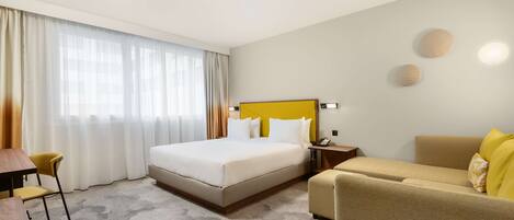 A hotel room with a large bed, a sofa, a desk, and a chair.