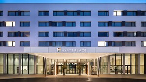 A modern hotel entrance with a glass facade, a sign reading "HYATT PLACE," and a covered entrance area with potted plants. - Hyatt Place Paris Charles de Gaulle Airport (Roissy-en-France)