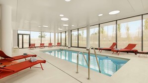 A modern indoor swimming pool with red loungers and large windows. - Hyatt Place Paris Charles de Gaulle Airport (Roissy-en-France)
