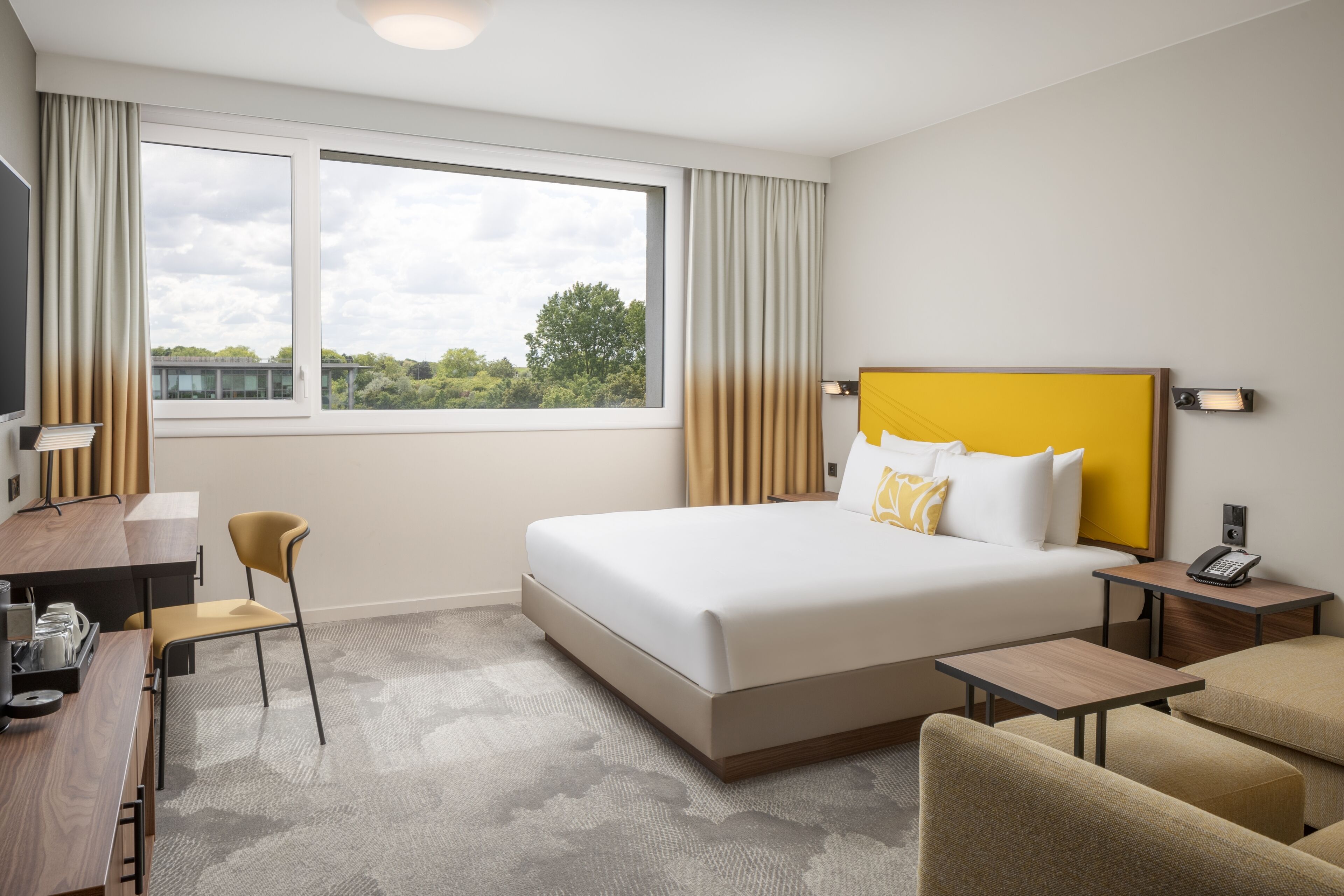 Ein Hotelzimmer mit einem großen Bett, einem Schreibtisch, einem Stuhl, einem kleinen Tisch und einem Nachttisch mit Telefon.