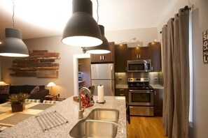 Una cocina moderna con electrodomésticos de acero inoxidable, encimera de granito e iluminación colgante.