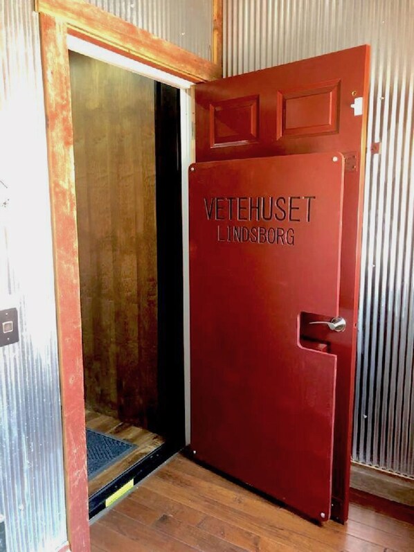 A red door with the inscription "VETESHUSET LINDSBORG" and a metal handle. - Vetehuset-Plantera Loft with Private Elevator (Lindsborg)
