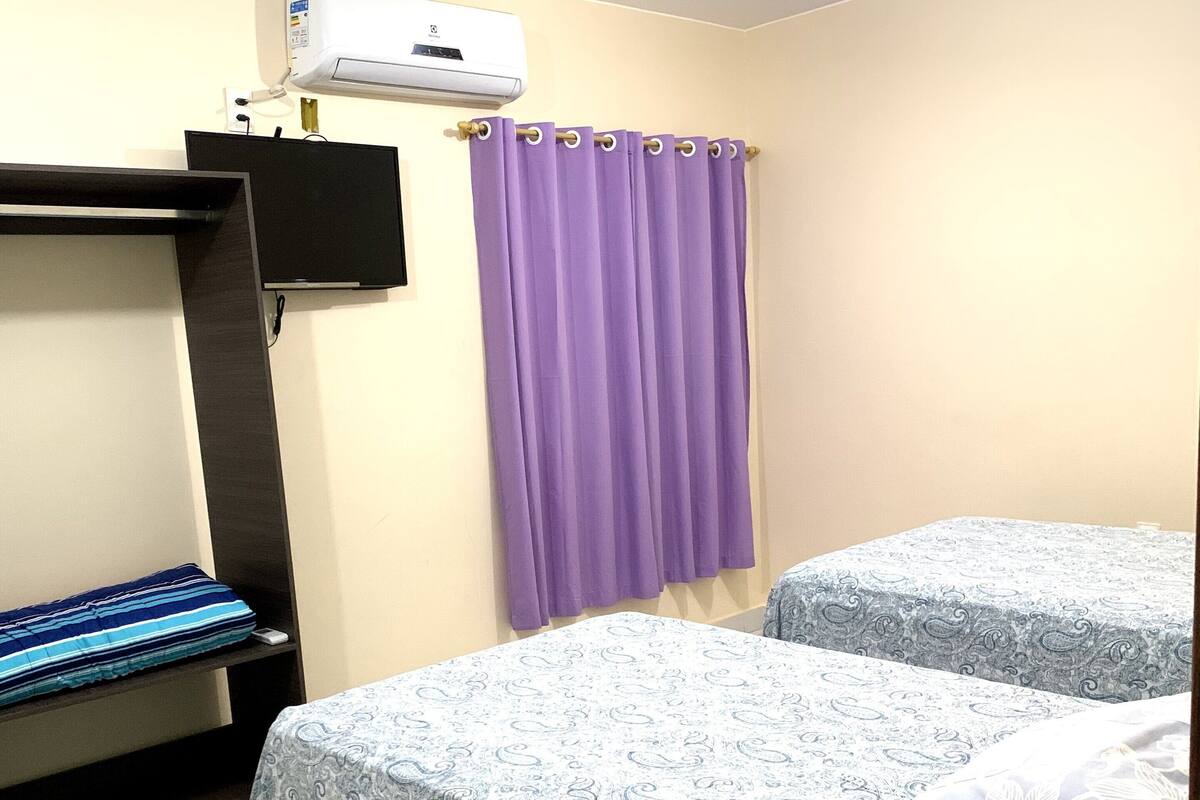 Una habitación con dos camas, televisión, aire acondicionado y una cortina morada.