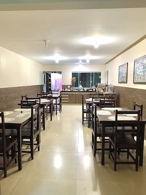 Un comedor amplio con varias mesas y sillas de madera, una barra con diversos artículos y cuadros en las paredes.