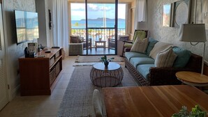 Sala de estar com sofá, mesa de centro, televisão e varanda com vista para o mar.