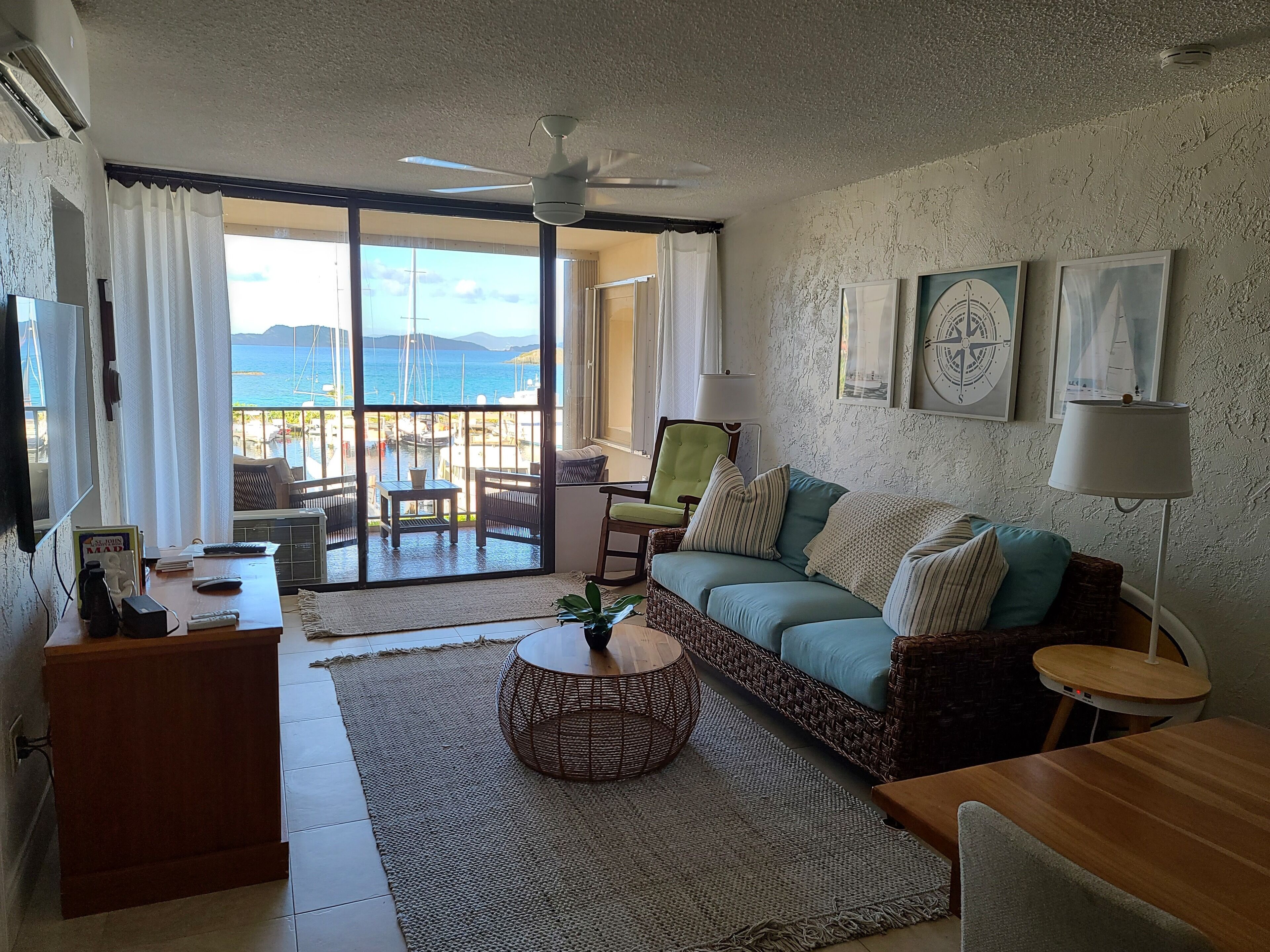 Ein Wohnzimmer mit einer Couch, einem Couchtisch, einem Fernseher und einem Balkon mit Meerblick.