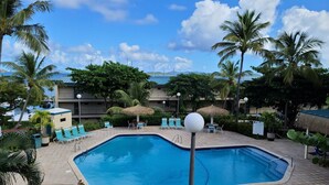 Piscina com espreguiçadeiras e guarda-sóis, cercada por palmeiras e um edifício com vista para o oceano.