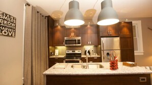 Uma cozinha moderna com armários de madeira, eletrodomésticos de aço inoxidável e iluminação pendente.