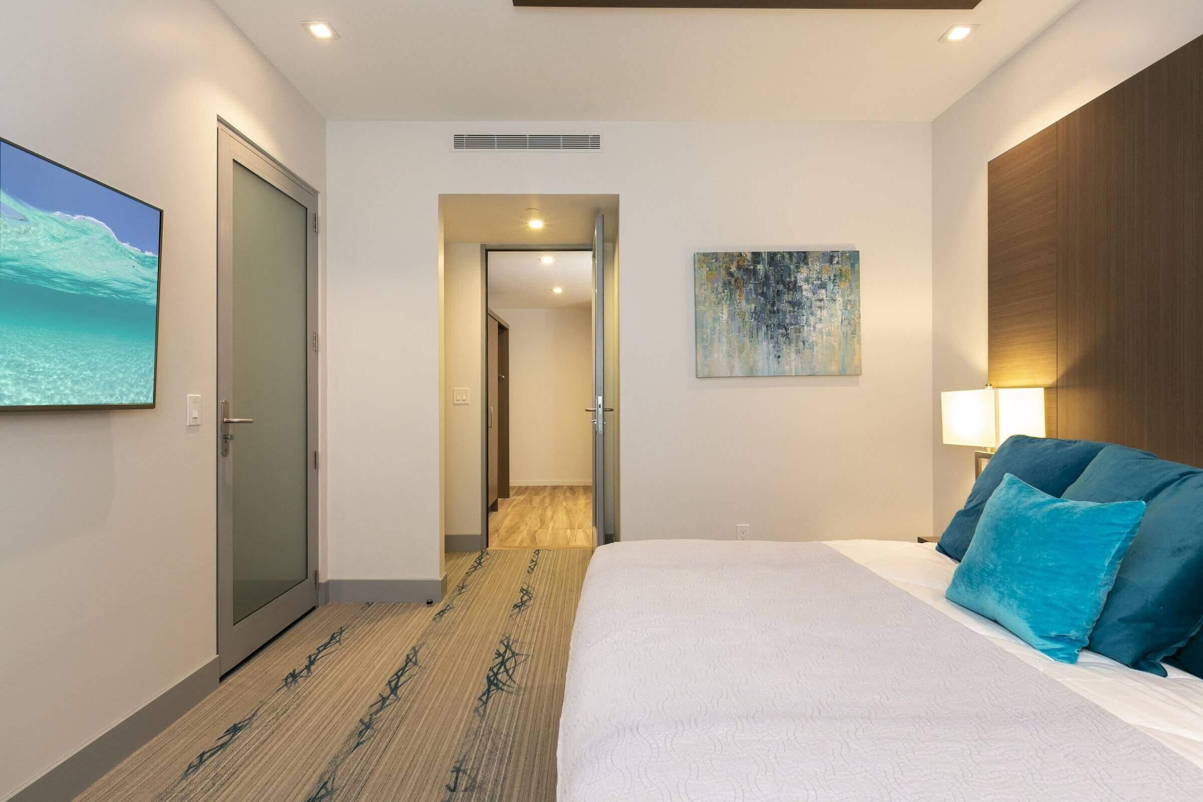 A hotel room with a bed, a painting, a lamp, and a view of the ocean.